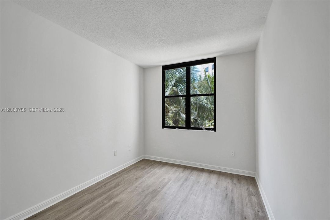 third bedroom, Interior space featuring neutral wall tones, wood-finish flooring, and a large window with a black frame