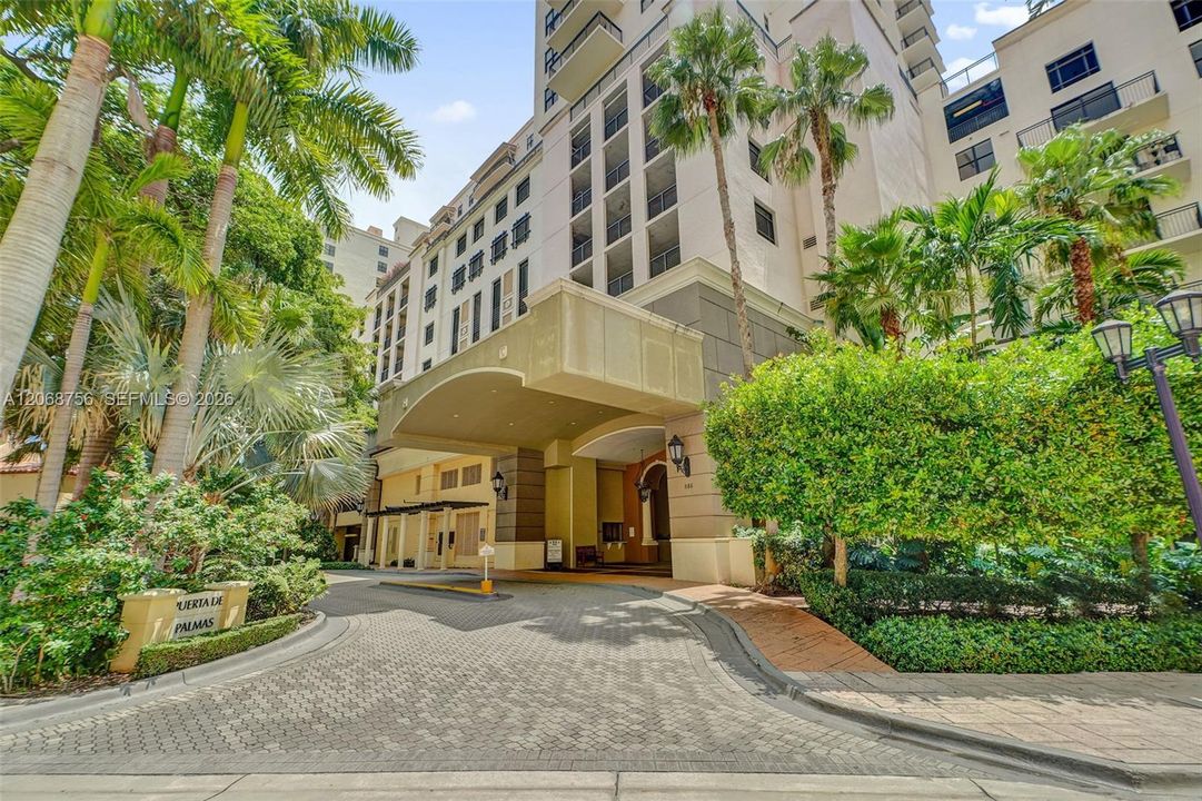 High-rise exterior featuring a grand porte-cochère, paver driveway, manicured landscaping with mature palms, and recessed balconies