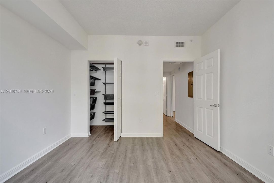 third bedroom, Neutral-toned wood-finish flooring, walk-in closet with built-in metal shelving, and six-panel interior doors