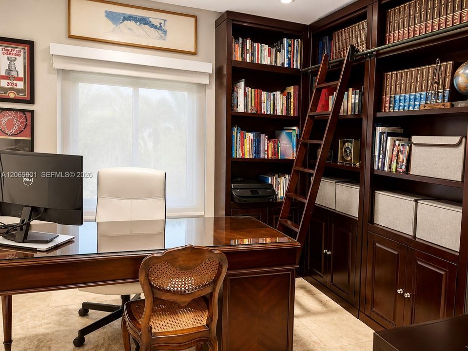 Private executive office designed for productivity and comfort. Features custom floor-to-ceiling built-in wood bookshelves with a rolling library ladder, extensive storage, and a spacious executive desk. Abundant natural light and marble floors create a bright, sophisticated workspace, ideal for working from home, studying, or managing a business in a quiet and elegant setting.