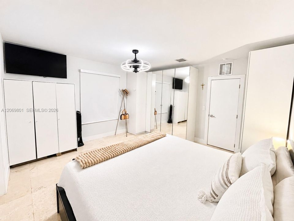 Spacious master bedroom featuring a walk-in closet, additional French-style closets, and a private master bathroom. The room offers generous storage, a bright neutral design, mirrored closet doors, and ample space for a large bed and furnishings, creating a comfortable and functional primary suite.