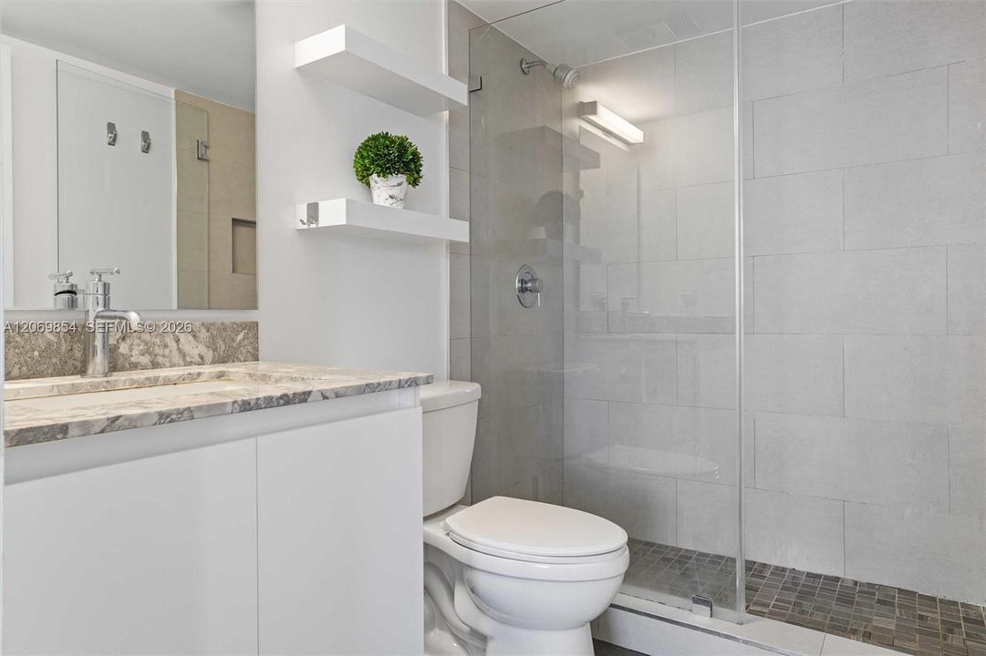 Beautifully updated master bathroom, where modern elegance meets everyday convenience. Featuring a spacious walk-in shower enclosed by sleek glass doors, this serene oasis is designed for relaxation. The contemporary vanity boasts a stunning marble countertop, complemented by a polished chrome faucet and ample storage below. Crisp white floating shelves add both style and function, providing the perfect space for décor or essentials. Large-format, neutral-toned tiles create a spa-inspired atmosphere