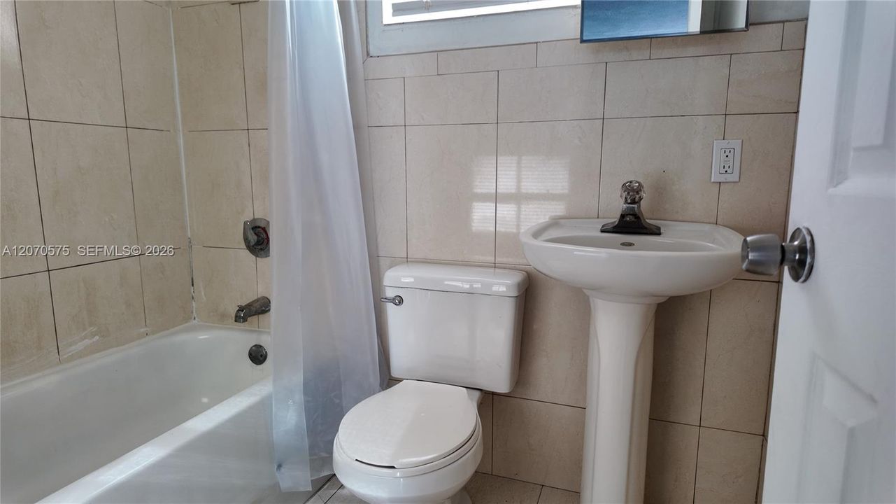 tiled walls, pedestal sink, mirror, and a window that brings in natural light and ventilation.