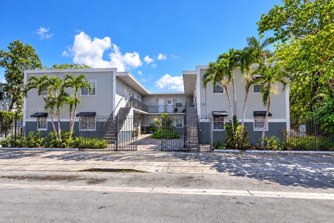Two-story multi-unit structure featuring a neutral exterior facade, decorative metal window awnings, and a gated perimeter fence