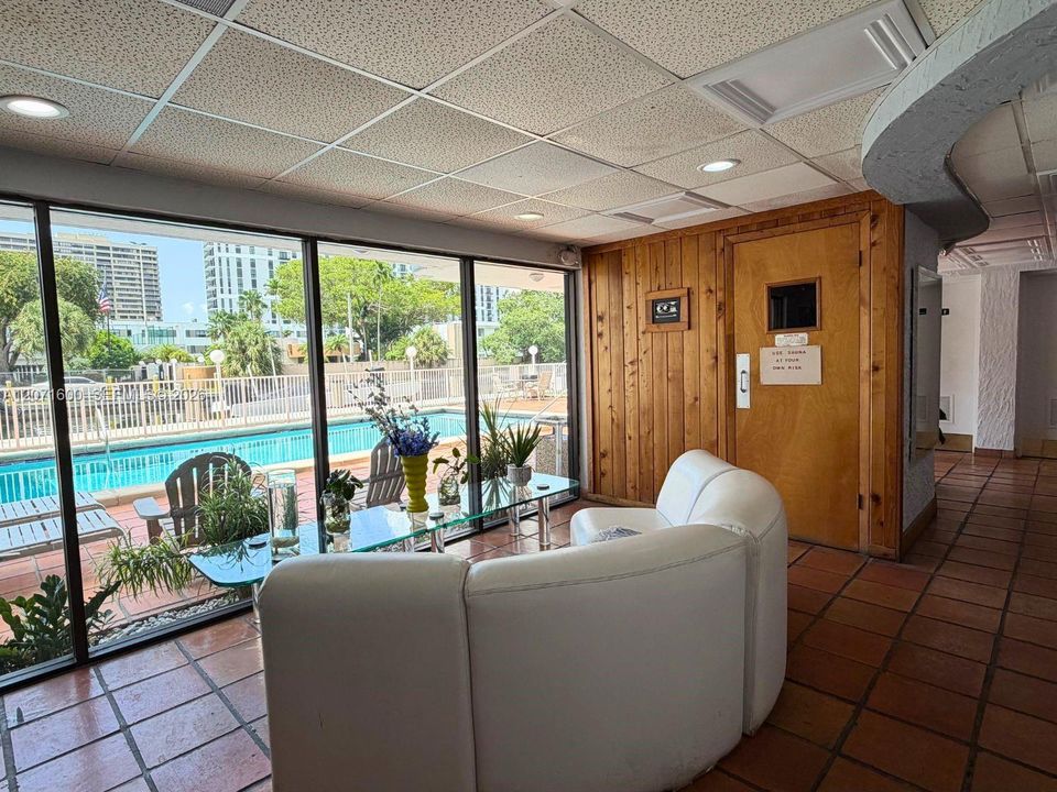 Inviting building lobby and lounge area featuring floor-to-ceiling windows overlooking the pool and community sauna access.