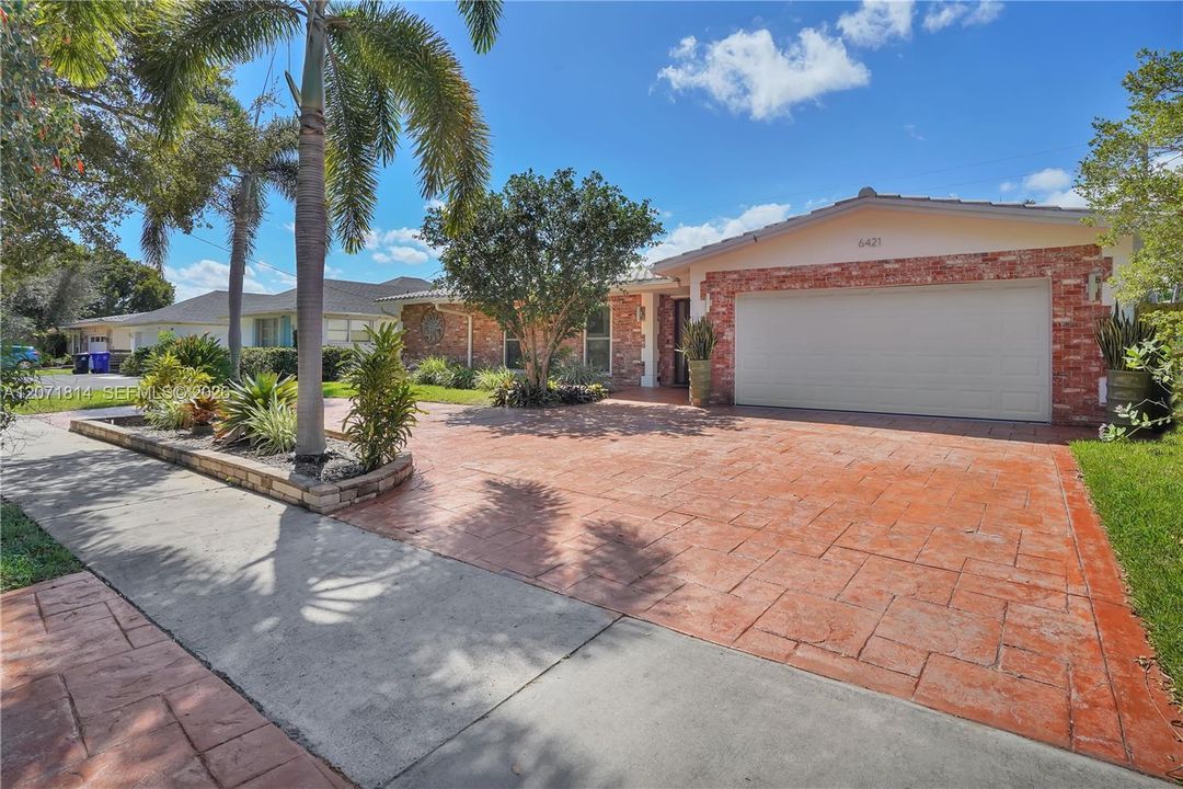 Beautifully landscaped curb appeal with paver driveway and lush greenery