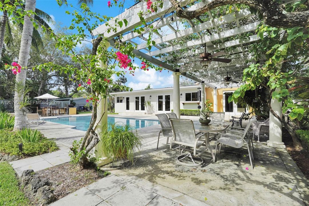 Alfresco dining area with shaded pergola overlooking sparkling pool.