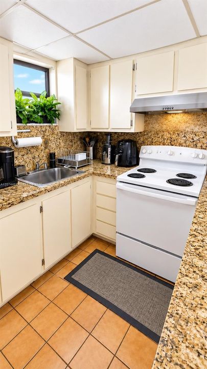Kitchen featuring stone-finish countertops, tile flooring, white cabinetry, a stainless steel undermount sink, and an integrated stainless steel range hood