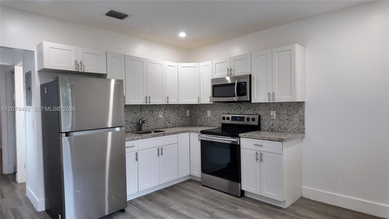 The kitchen keeps things crisp and functional with white shaker-style cabinetry, granite countertops and stainless-steel appliances, including the refrigerator, range and microwave.