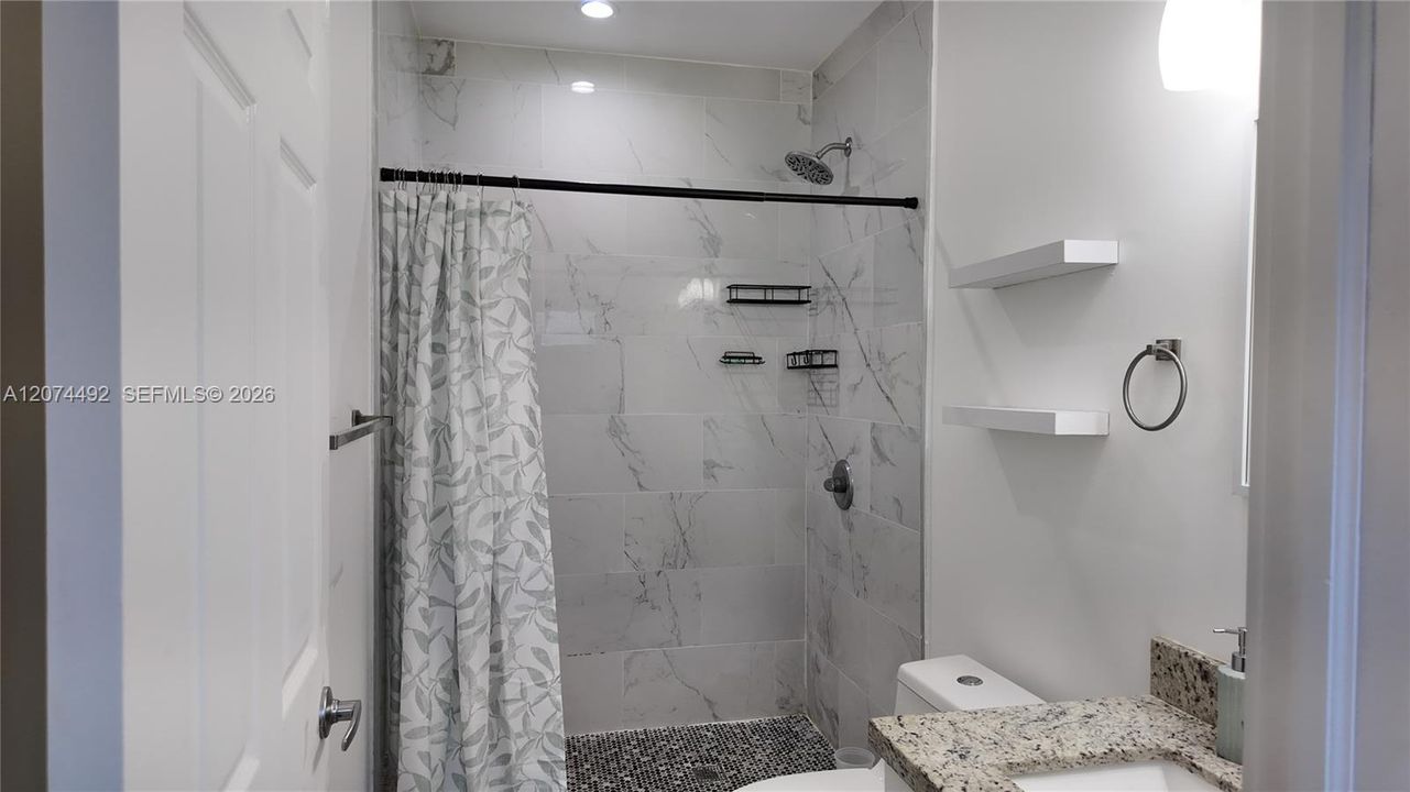 The shower is finished with large marble-look tile, a rainfall-style showerhead and contrasting black details.