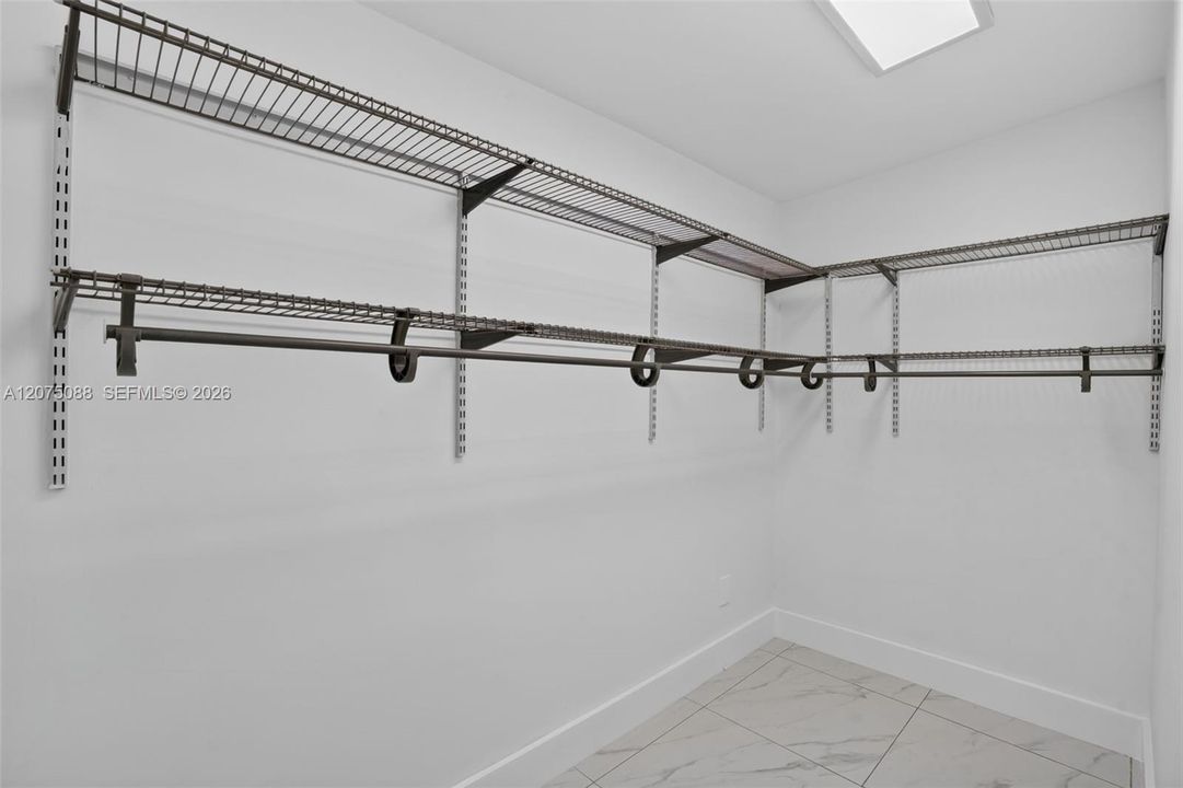 Walk-in closet featuring multi-tiered wire shelving, integrated garment rods, recessed ceiling lighting, and large-format tile flooring