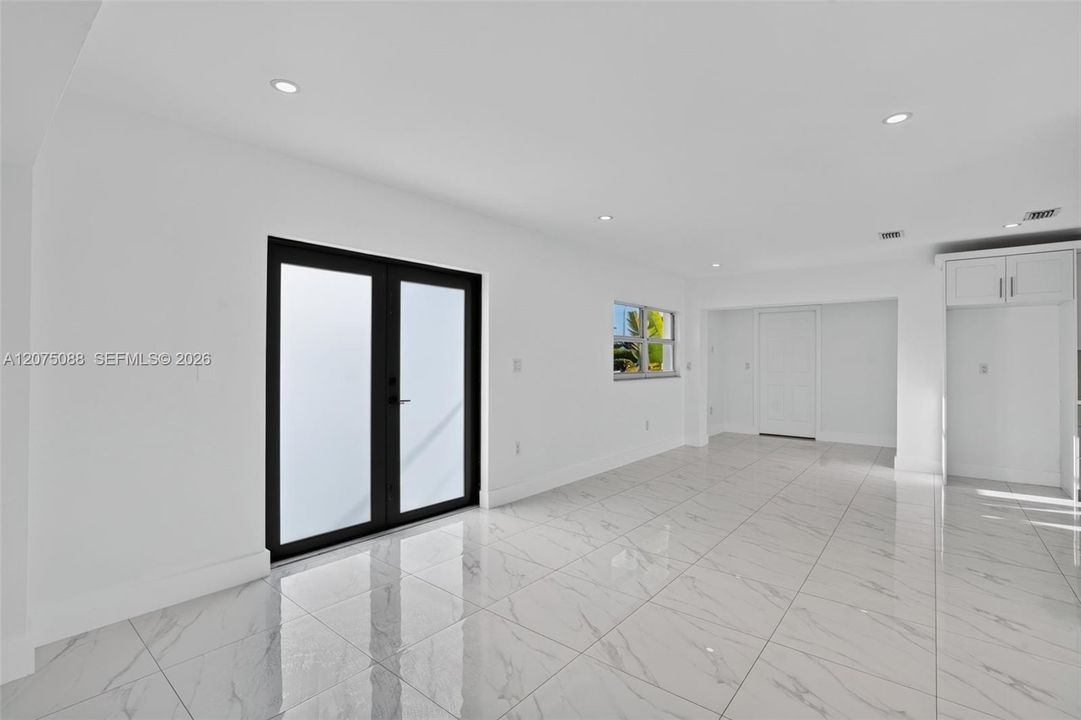 Interior space featuring large-format tile flooring, double glass entry doors with black frames, recessed ceiling lighting, and custom built-in cabinetry