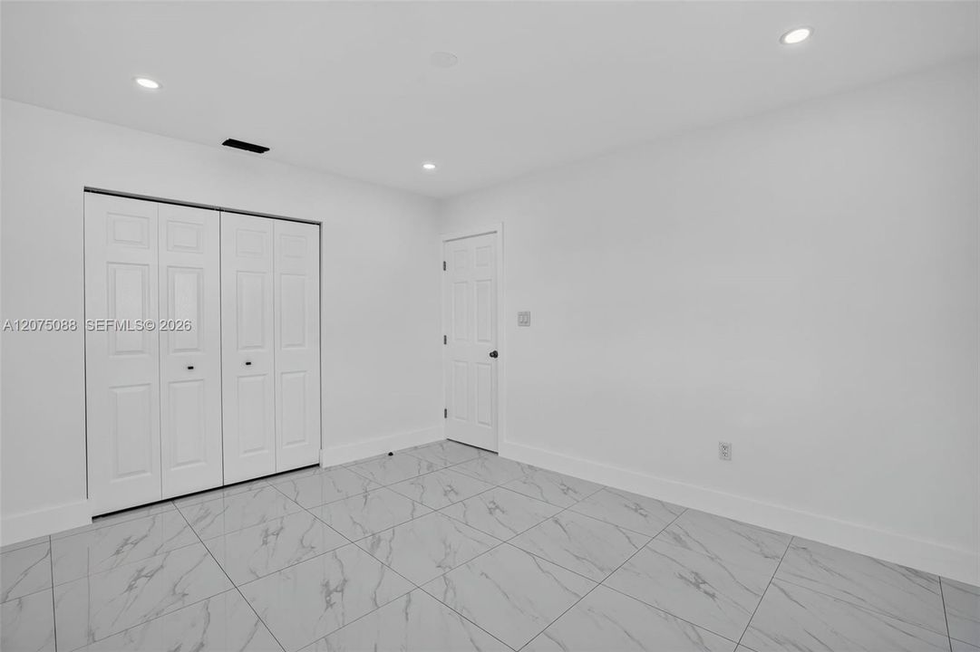 Neutral-toned interior featuring large-format tile flooring with a veined pattern, recessed ceiling lighting, and a double-panel closet with bifold doors