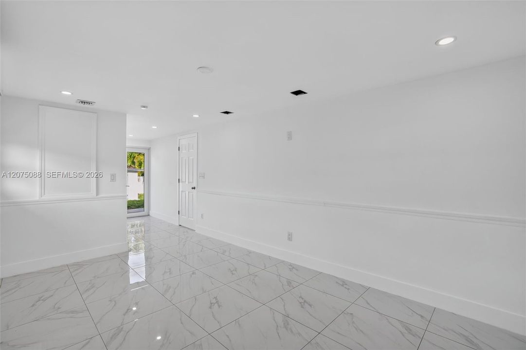 Large-format tile flooring with a neutral-toned veining pattern, crisp white walls, recessed ceiling lighting, and crisp white chair rail molding