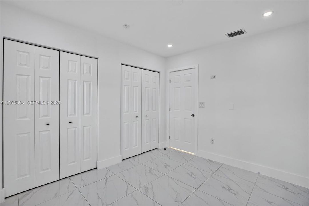 Room featuring large-format tile flooring, dual sets of bi-fold closet doors, a classic interior door, and recessed lighting