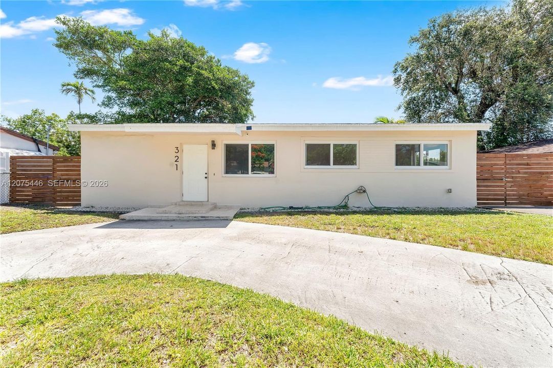 Crisp white ranch home featuring updated windows, modern wood privacy fencing on both sides, and a wide concrete driveway with mature shade trees framing the property.