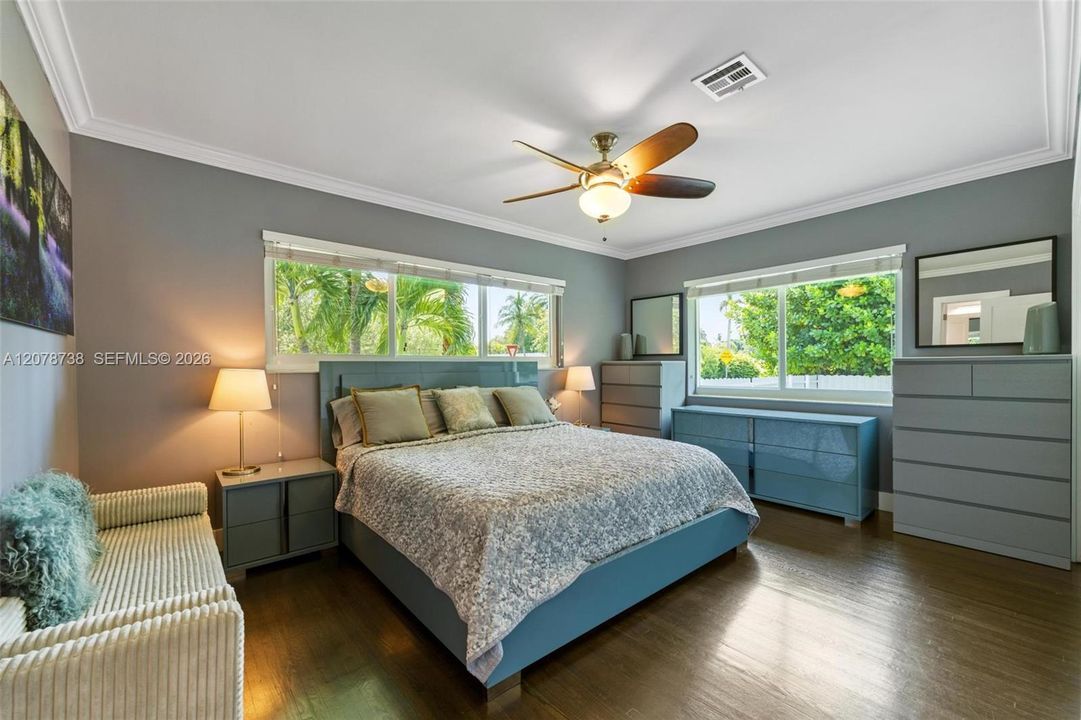 Leaving the shared spaces behind, the primary bedroom introduces a quieter mood with soft tones, warm floors, and abundant natural light.