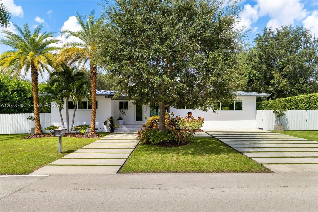 A modern metal roof, crisp white exterior, oversized stepping-stone driveway and lush greenery create a contemporary first impression without losing the warmth of a true neighborhood home.