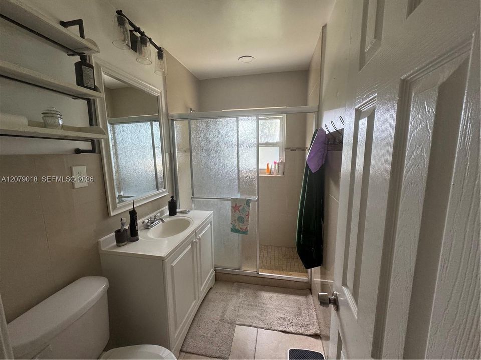 Bathroom featuring a single-sink vanity with white cabinetry, a framed wall mirror, a glass-enclosed shower, and neutral-tone tile flooring