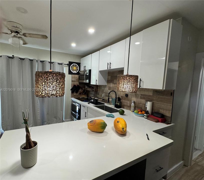 Kitchen featuring white gloss cabinetry, quartz countertop, textured tile backsplash, and dual woven-shade pendant lights