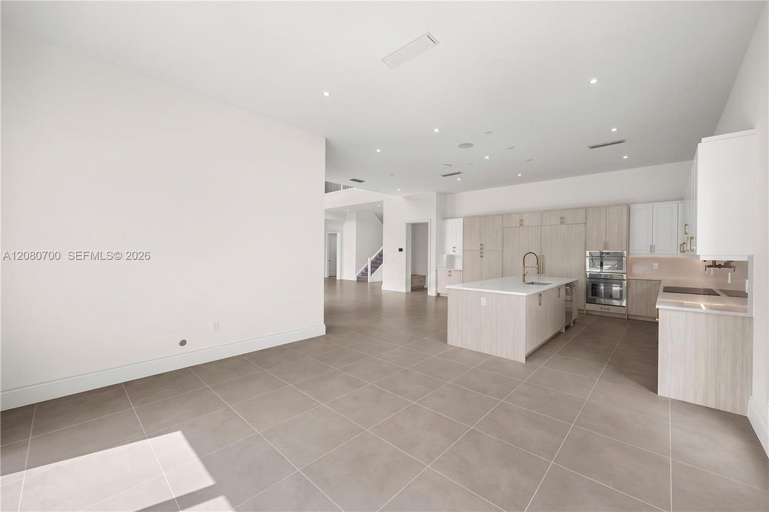 Spacious open-concept area featuring a gourmet kitchen with a central island, integrated appliances, recessed lighting, and large format tile flooring
