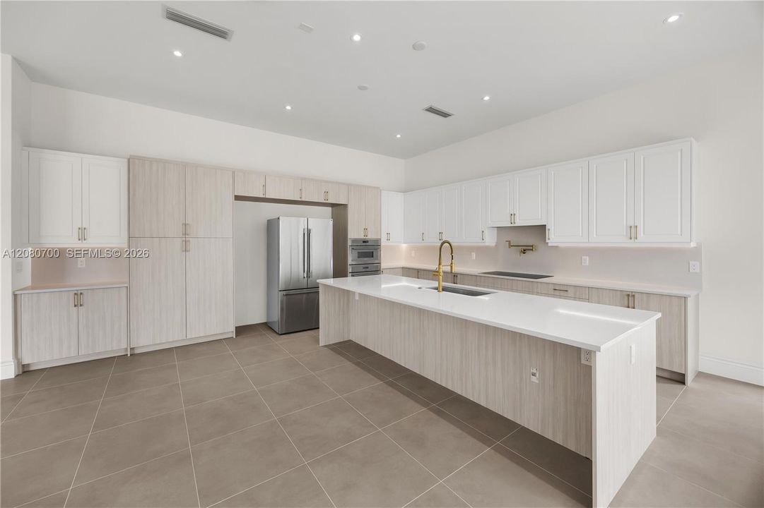 Spacious kitchen featuring an expansive island, stainless steel appliances, integrated cooktop, abundant cabinetry, and tile flooring