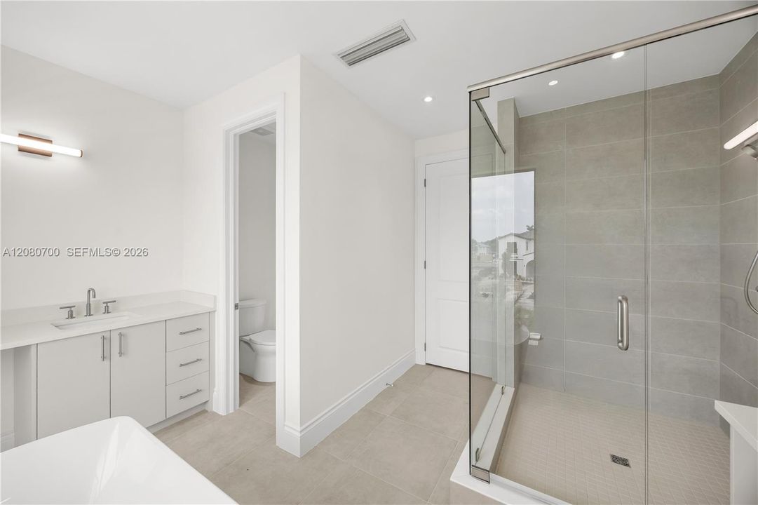 Walk-in shower with clear glass enclosure and light-toned tile surround, single vanity with light cabinetry and solid surface countertop, and tile flooring