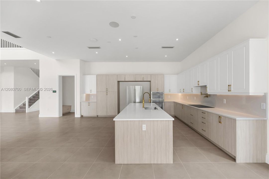 Spacious kitchen featuring an expansive island with a built-in sink, stainless steel appliances, extensive cabinetry with integrated lighting, and neutral-toned floor tiling