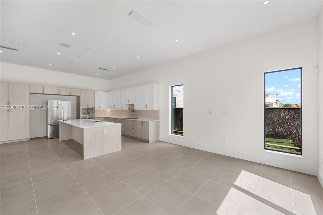 Expansive open-concept space featuring large format floor tiling, a kitchen island with a built-in sink, recessed lighting, and rectangular windows