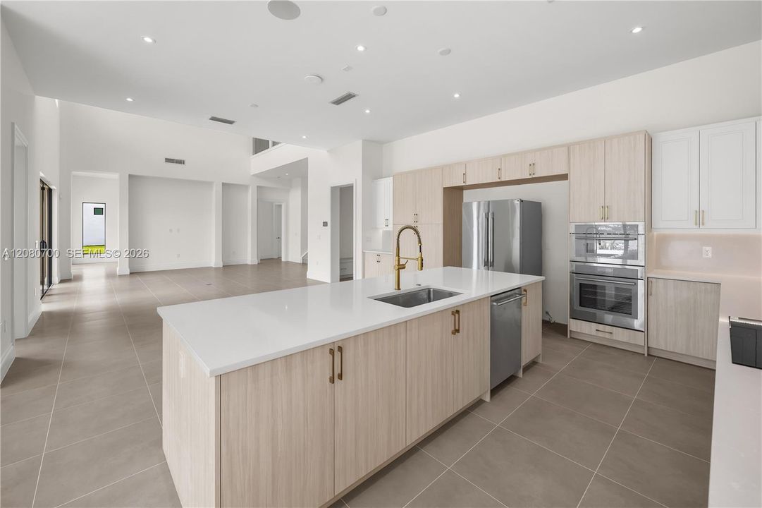 Modern kitchen featuring an expansive center island with an undermount sink and brass faucet, stainless steel appliances, and integrated cabinetry