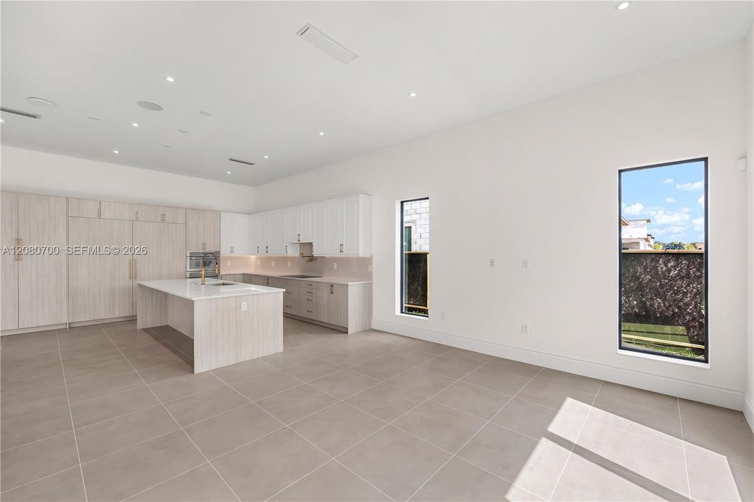 Open-concept kitchen and living area featuring large format tile flooring, a central island with an integrated sink, built-in appliances, and recessed lighting