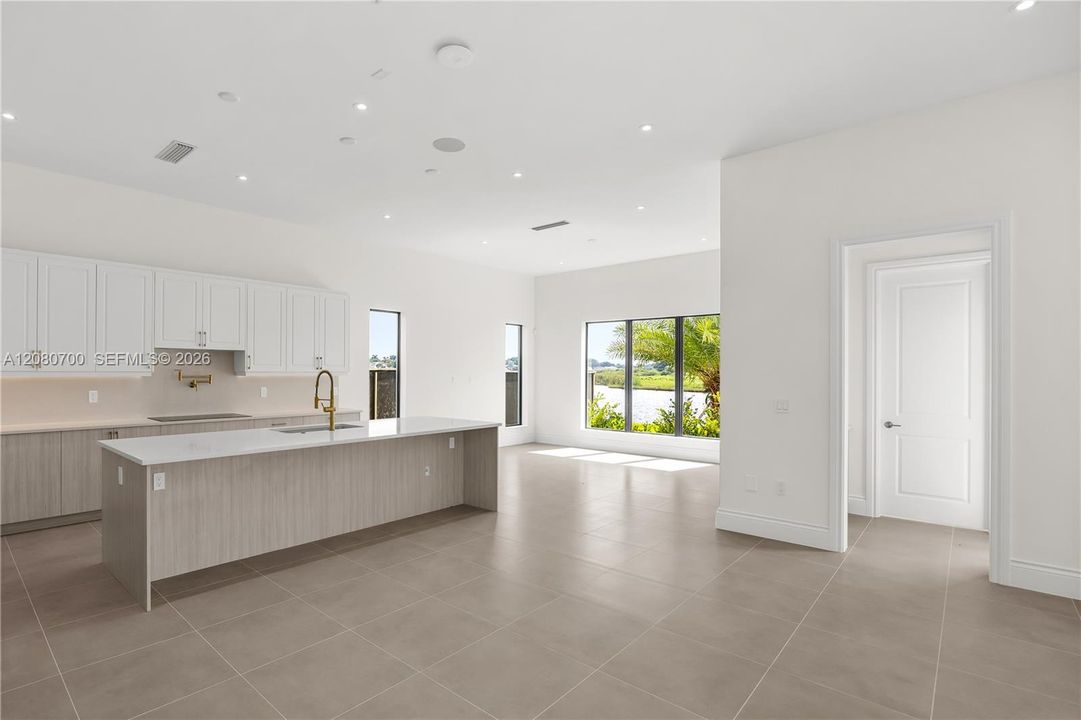 Expansive kitchen island with a gold-finish faucet, white shaker-style cabinetry, and integrated ceiling lighting