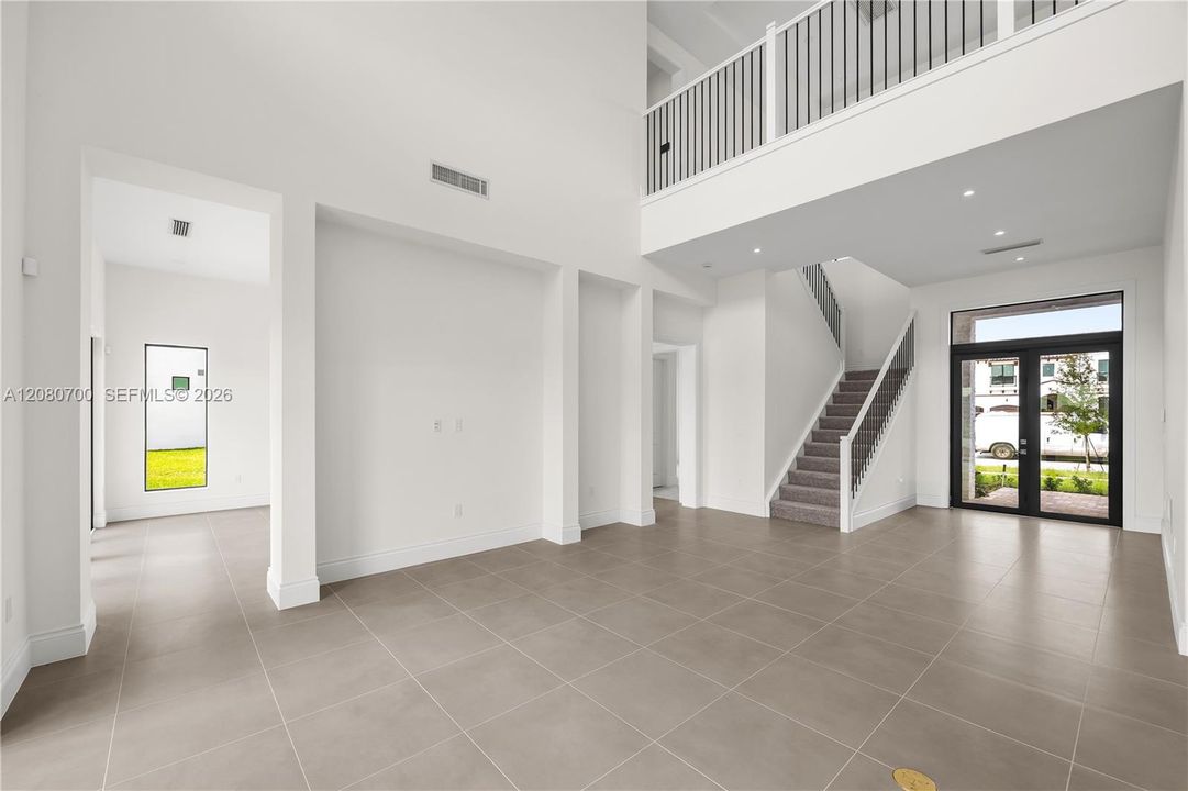 Two-story foyer with high ceilings, large format tile flooring, a modern staircase with metal balusters, and a glass-paneled entry door
