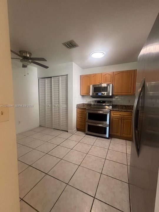 Kitchen featuring wood cabinetry, stone countertops, stainless steel appliances, ceramic tile flooring, and closet storage with louvered doors