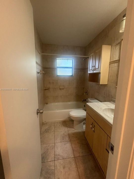 Bathroom featuring floor-to-ceiling tile, vanity cabinet with integrated countertop, wall-mounted medicine cabinet, and tub-shower combination