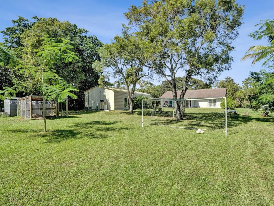 Expansive lawn featuring mature trees, a detached storage building, and a fenced enclosure