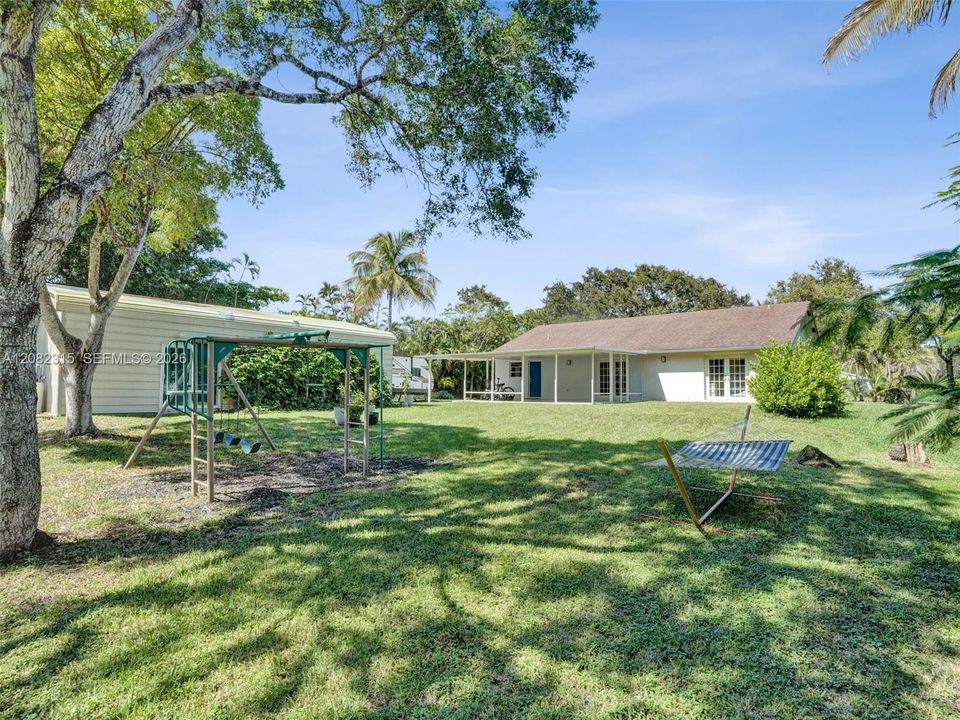 Expansive backyard featuring a sprawling lawn, mature trees, a detached storage structure, and a covered rear patio