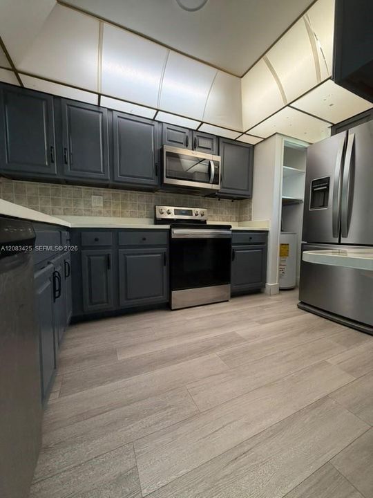Kitchen featuring dark-toned cabinetry, stainless steel appliances, wood-finish flooring, and a coffered ceiling with inset lighting