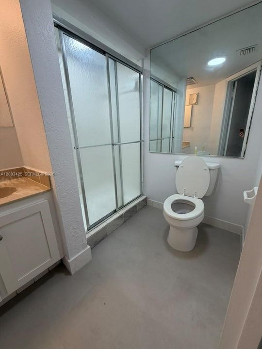 Bathroom featuring a walk-in shower with a sliding glass enclosure, white cabinetry, a neutral-toned countertop, and an expansive wall-mounted mirror