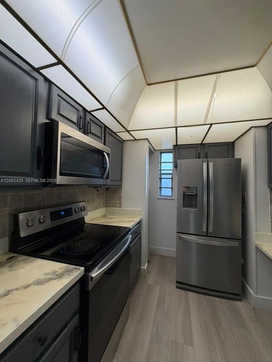 Kitchen featuring dark-toned cabinetry, light-toned countertops with a marble-patterned finish, wood-finish flooring, and stainless steel appliances