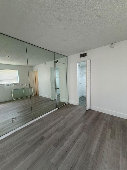 Wood-finish flooring, full-wall mirrored paneling, and closet with louvered door