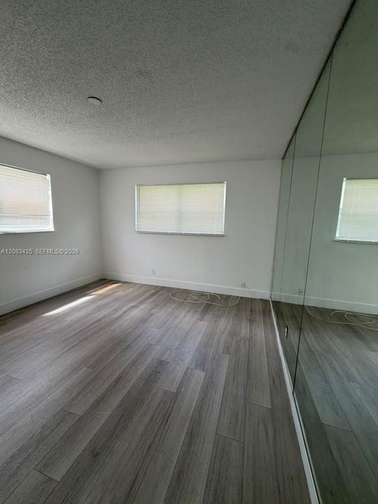 Neutral-toned interior featuring wood-finish flooring, full-height mirrored closet doors, and multiple windows