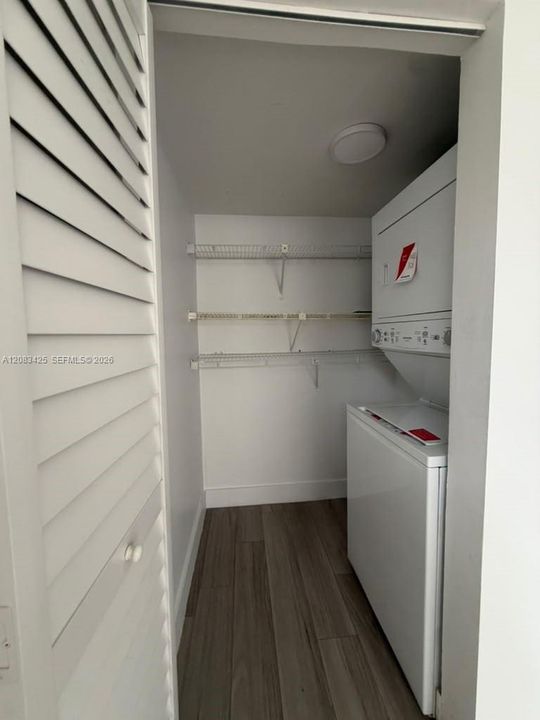 Laundry closet featuring louvered bi-fold doors, wood-finish flooring, stacked laundry appliance, and three levels of built-in wire shelving