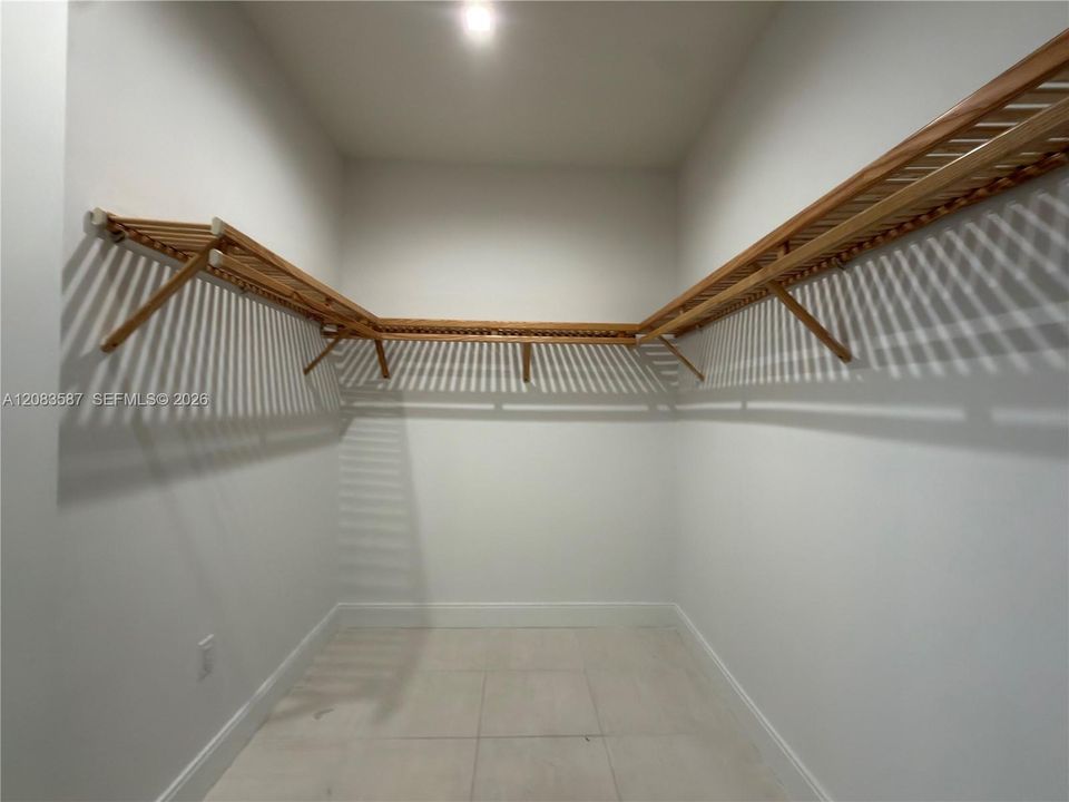 Walk-in closet featuring light-toned tile flooring and tiered wooden shelving with integrated hanging rods
