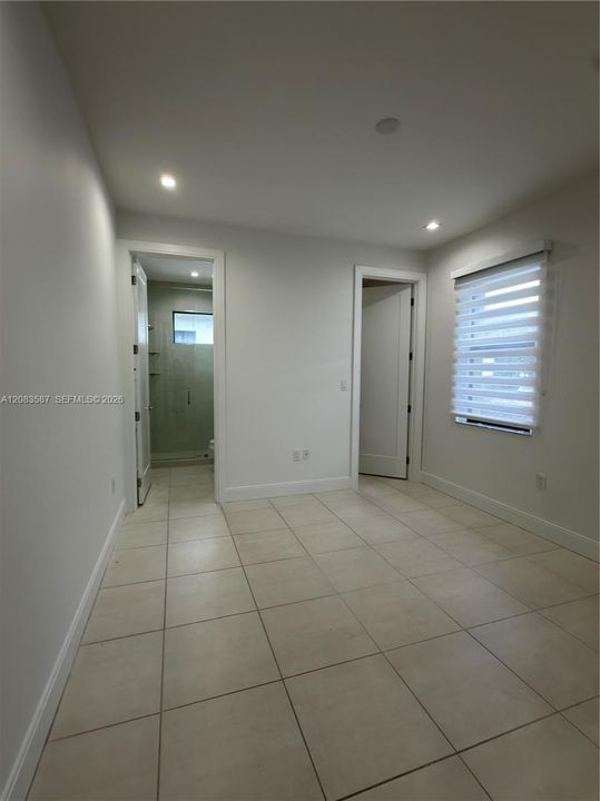 Bright hallway featuring neutral tile flooring, recessed ceiling lighting, and multiple doorways providing access to adjoining spaces