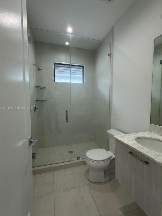 Walk-in shower with frameless glass enclosure, tiled surround, and integrated shelving, featuring a vanity with a stone-top counter and large wall-mounted mirror