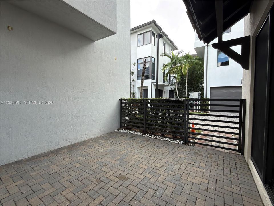 Private patio featuring paver flooring, a horizontal slat metal fence, and exterior stucco finishes