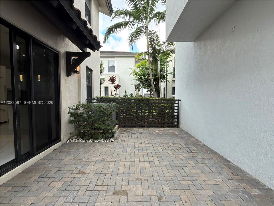 Paved patio featuring herringbone-patterned masonry, metal privacy fencing, and exterior sliding glass doors