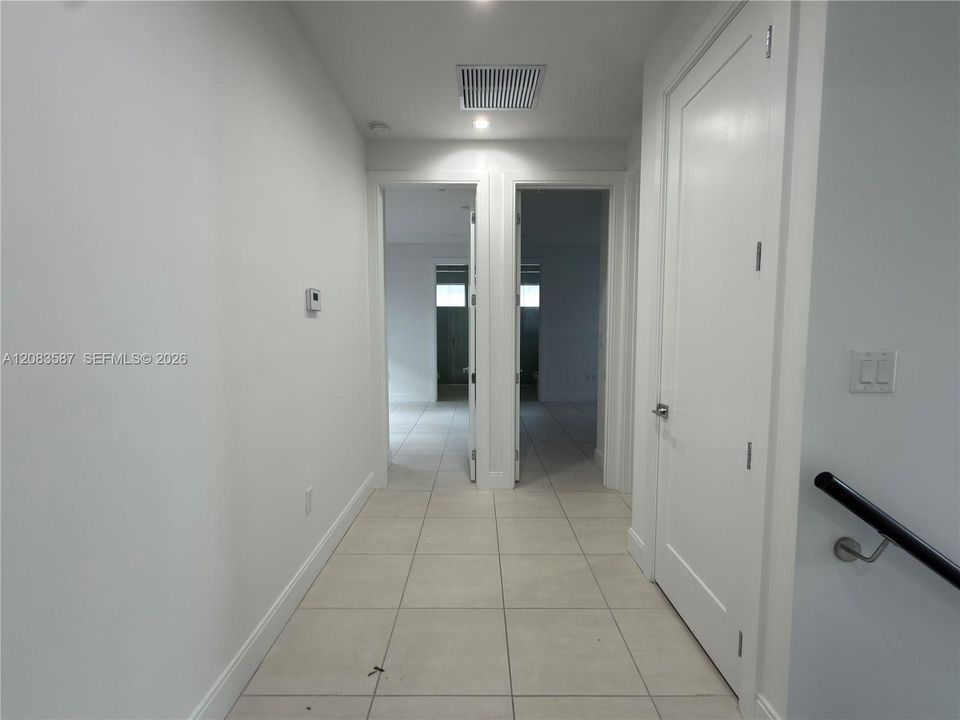 Hallway featuring neutral large-format tile flooring, crisp white walls, recessed ceiling lighting, and solid-core interior doors with satin nickel hardware