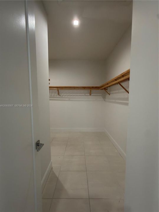 Walk-in storage space featuring large-format ceramic tile flooring, neutral walls, and integrated wooden shelving